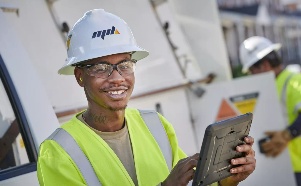 Man smiling in a hard hat, holding a tablet